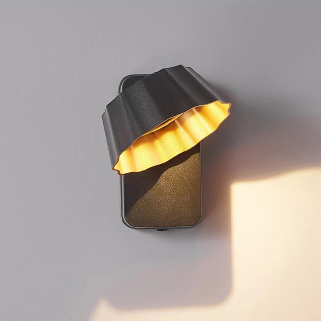 Black wall-mounted light with gold interior creating dramatic shadow and light patterns