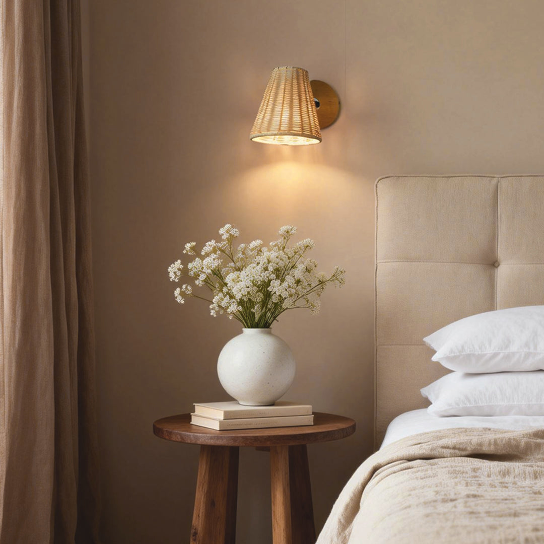 Minimalist Japanese wall light featuring a natural rattan shade, illuminating a bedside table with a vase of flowers.