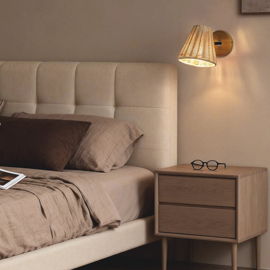 Elegant Japanese wall light with woven rattan shade, casting warm light above a cozy bedroom nightstand and tufted headboard.
