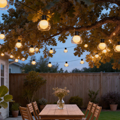 LED globe string lights suspended from a large tree above an outdoor table, adding soft ambient lighting to the garden.