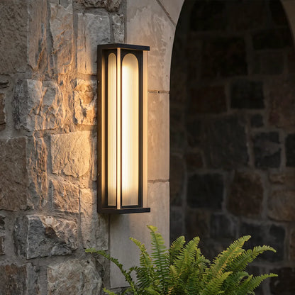 Modern outdoor wall sconce with warm lighting on stone wall beside garden plants