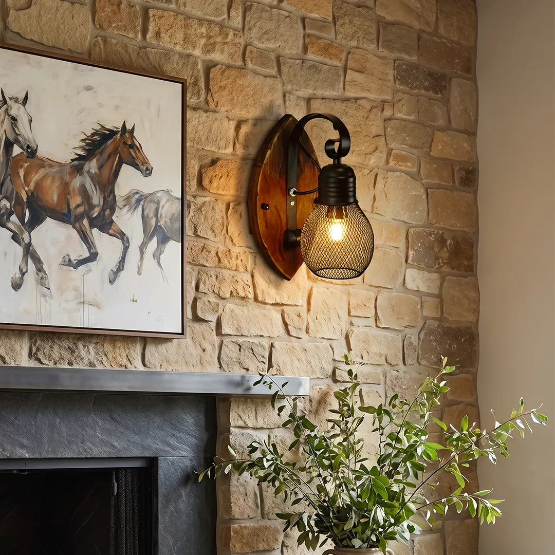 Rustic farmhouse wall sconce with a warm Edison-style bulb, black curved arm, and round wood backplate mounted on a stone fireplace wall.