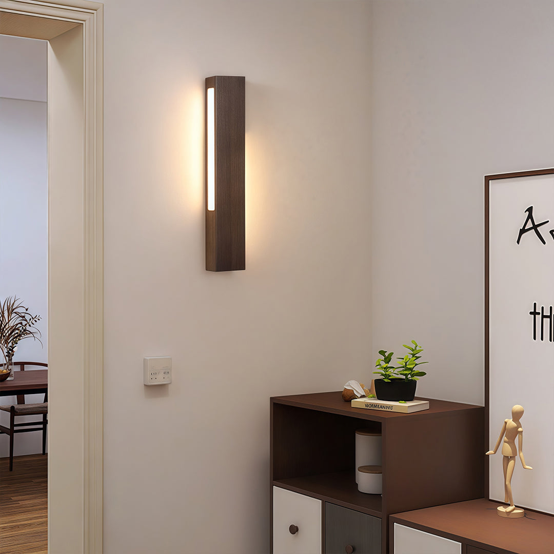 Slim Japanese wall light with a long dark wooden frame, mounted next to a doorway to provide discreet hallway lighting.