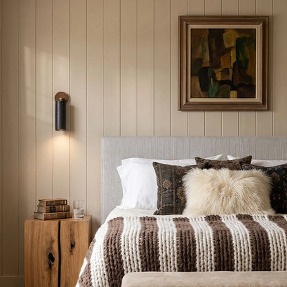 Spotlight wall lights mounted beside a bed in a warm neutral bedroom with wood furniture.